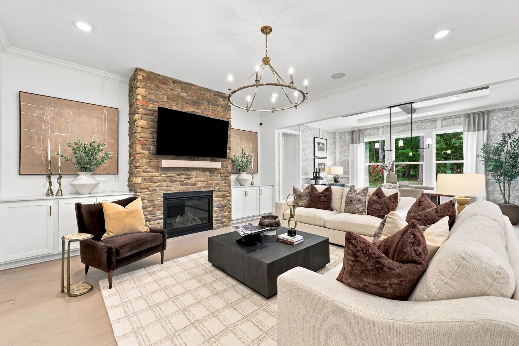 Davidson Homes great room with a stone fireplace, brass chandelier and views into a tree-lined sunroom
